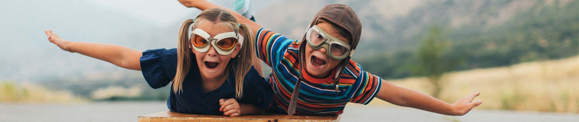Two kids wearing goggles pretending to be airplanes